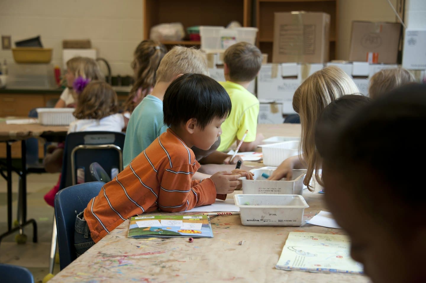 Bambini diversi lavorano a progetti artistici a un tavolo di classe.